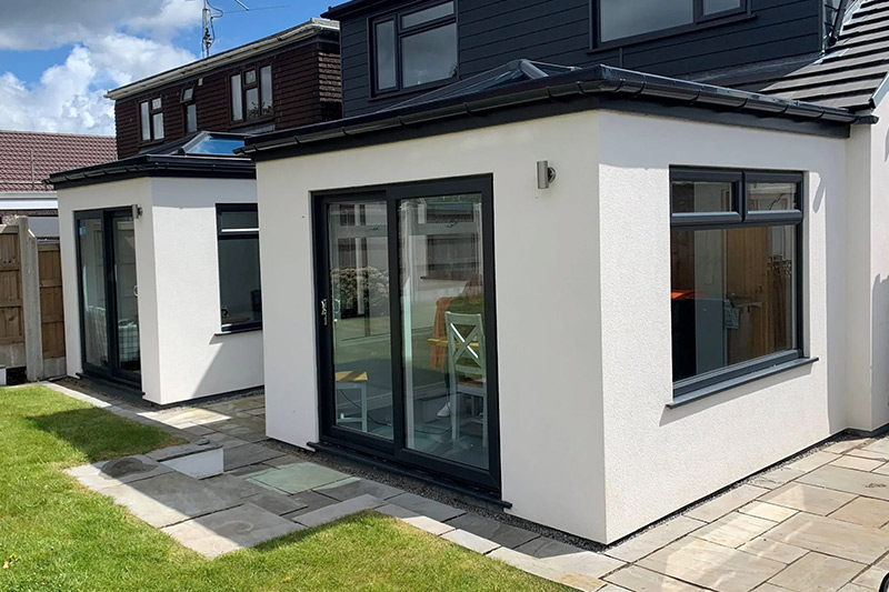 Modern white home extension with large windows and patio doors leading to a garden.