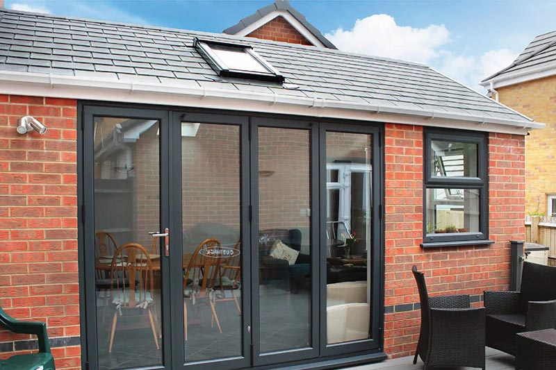 Brick extension with gray bi-fold doors and skylight, opening to a patio area.