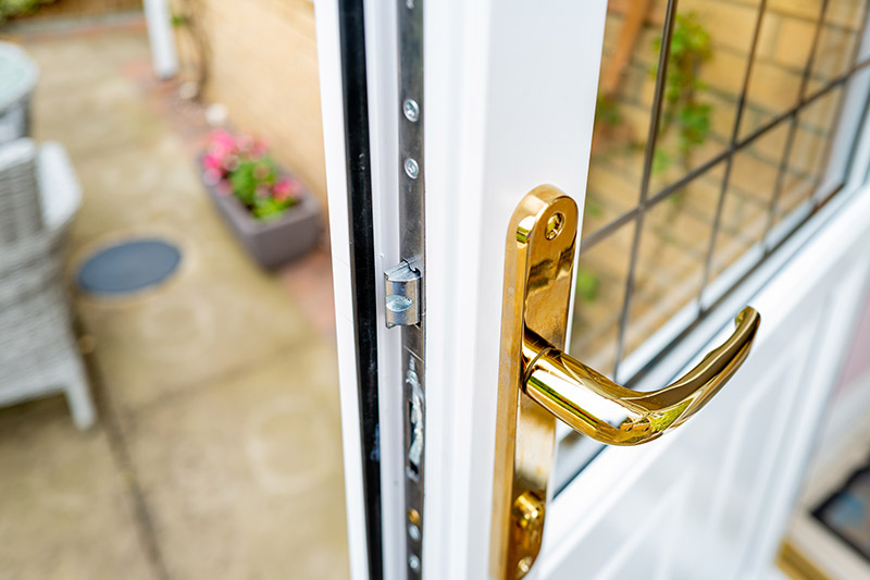 Close-up of a gold back door handle on a white UPVC door with a view of a patio area in the background